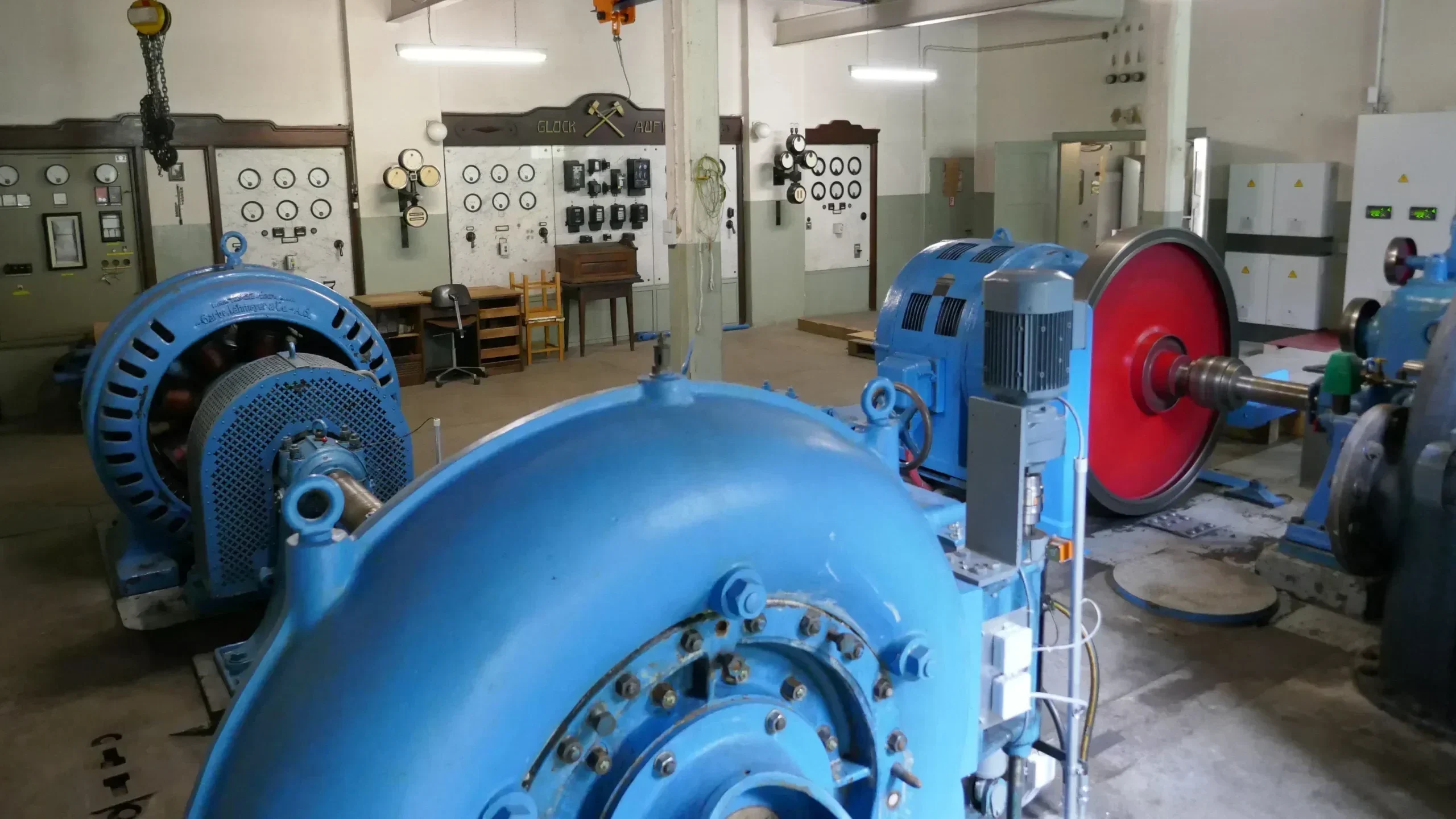 alte Schaltwarte mit Synchroniskop Blaue Francis-Spiralturbinen mit 6-kV-Generatoren und statischer Erregung, im Hintergrund eine alte Schaltwarte mit Synchronoskop sowie Anzeigen für kW, Strom und Erregerstrom.