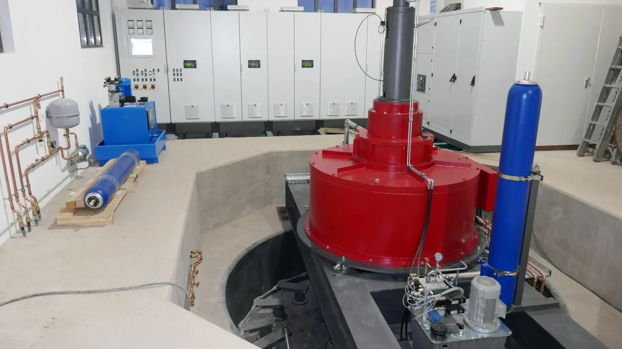 Kaplanturbine mit rotem PMG-Generator in einem runden Betonbecken, im Hintergrund eine weiße Schaltschrankzeile für drei Turbinen