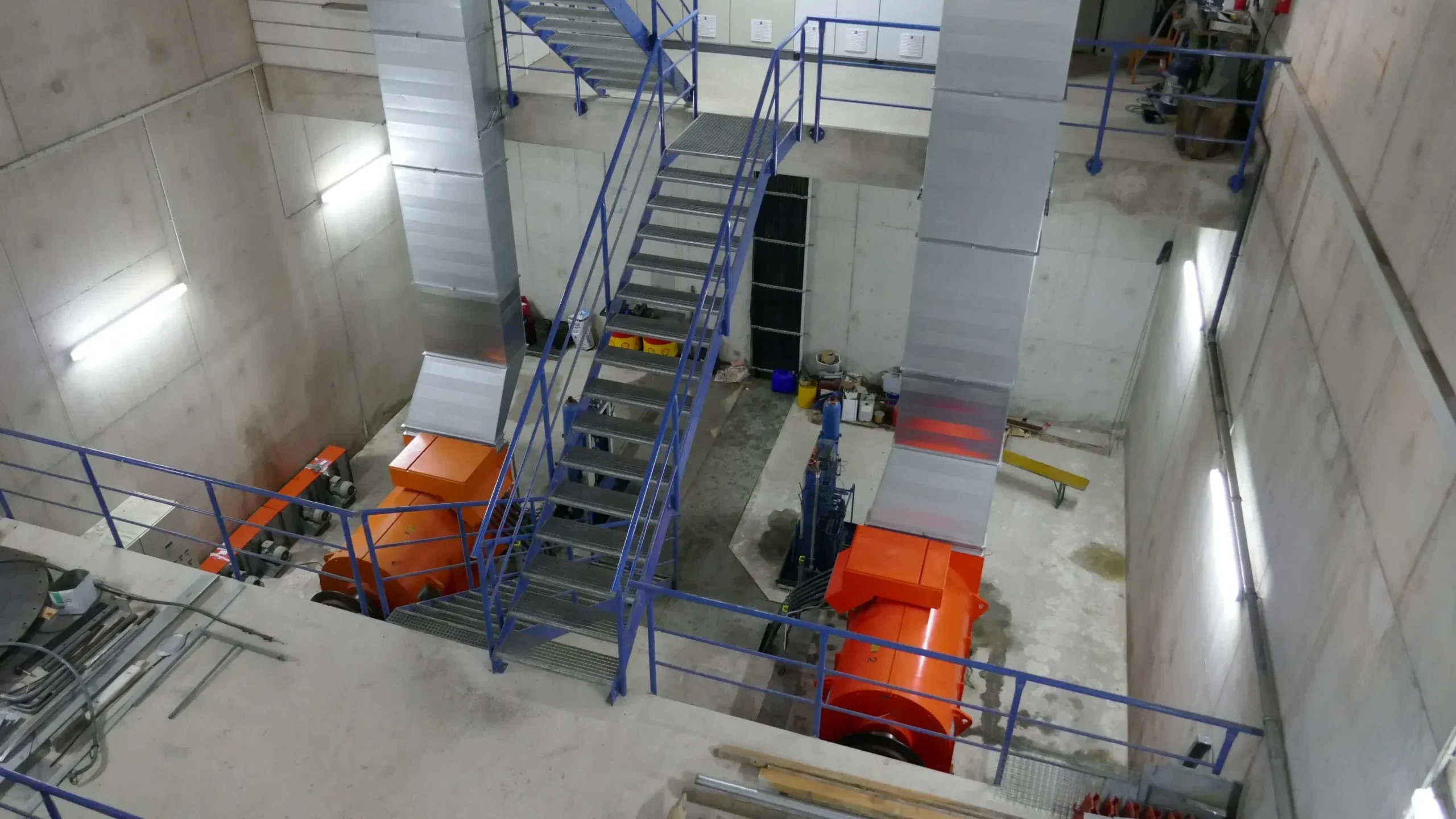 Blick in einer Maschinenhalle in die Tiefe auf zwei Kössler Rohrturbinen und einer blauen Metalltreppe in der Mitte