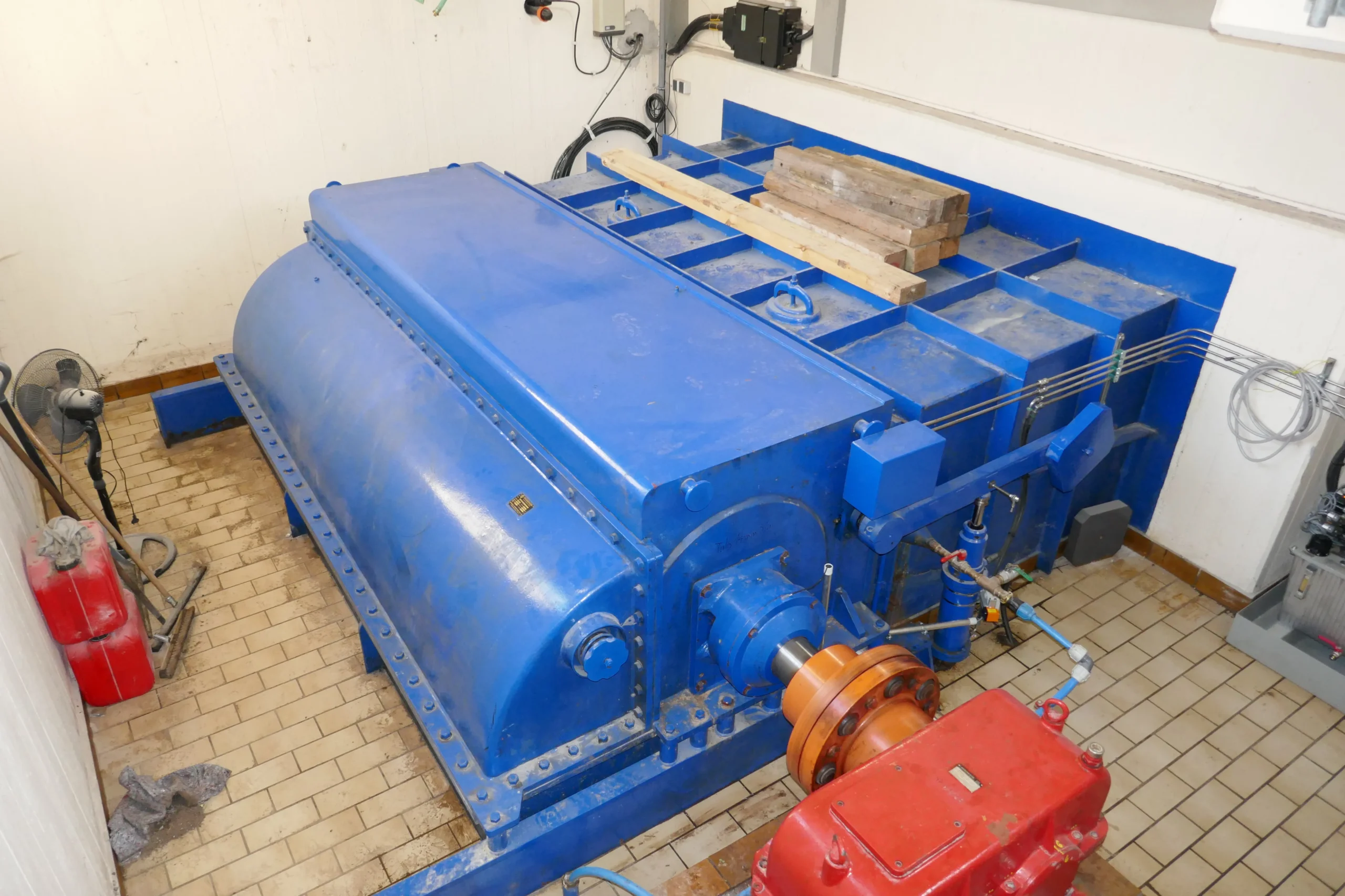 Ossberger Durchströmturbine Altensteig Blaue Ossberger Durchströmturbine in einem Raum mit beige gefliestem Boden und rotem Getriebe.
