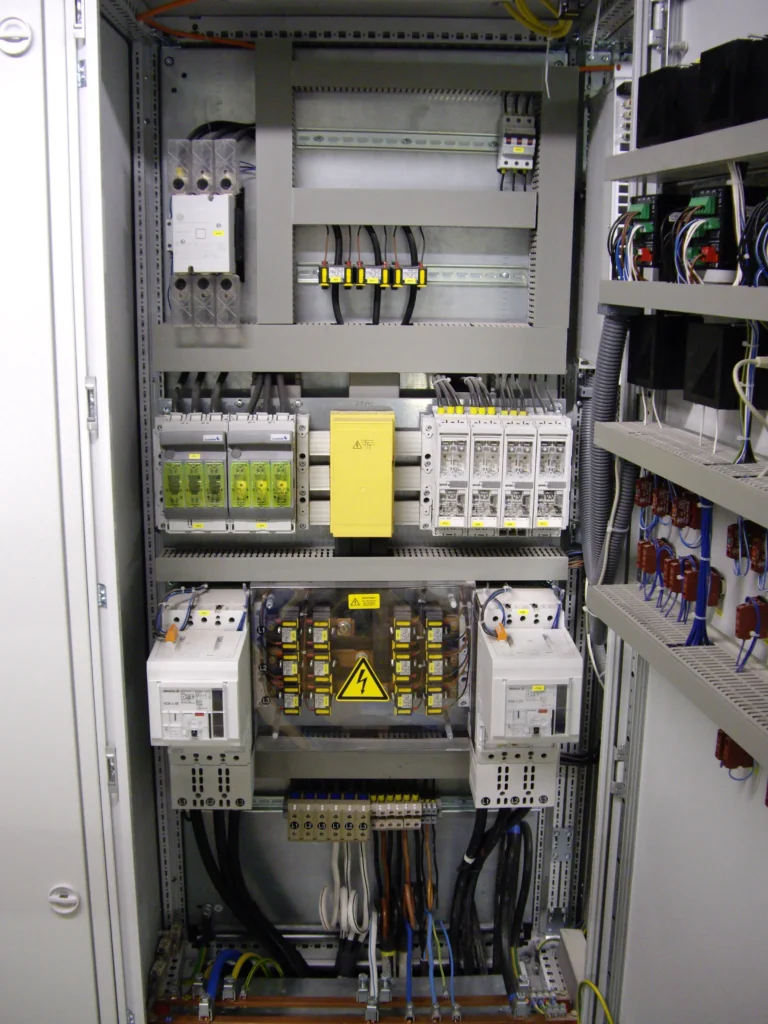 Leistungschrank für Insel- und Netzparallelbetrieb Der geöffnete Leistungsschrank zeigt links den Netzschalter, rechts den Generatorschalter und in der Mitte die Stromschiene mit Stromabgängen zu den Spritzgußmaschinen.