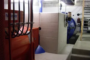 Große Kaplanturbine in einer Maschinenhalle mit Deckenkran, rechts im Bild Blick zum Leitstand, vorne im Bild ein blauer Hydrauliktank mit Pumpen und Sensoren.