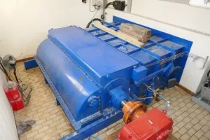 Große Kaplanturbine in einer Maschinenhalle mit Deckenkran, rechts im Bild Blick zum Leitstand, vorne im Bild ein blauer Hydrauliktank mit Pumpen und Sensoren.